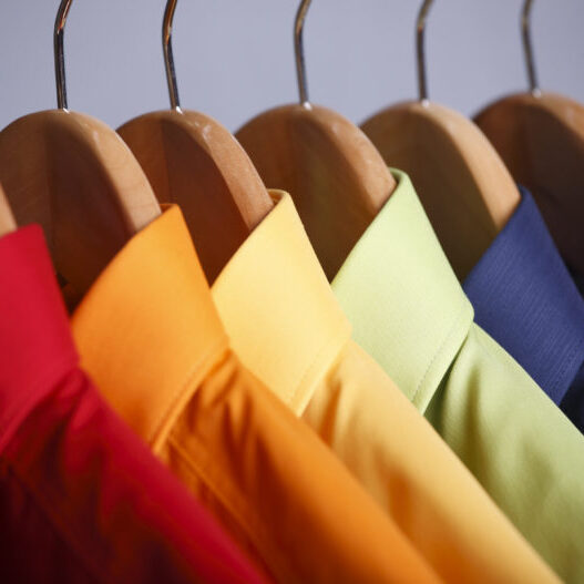 Rainbow colored shirts on hangers.